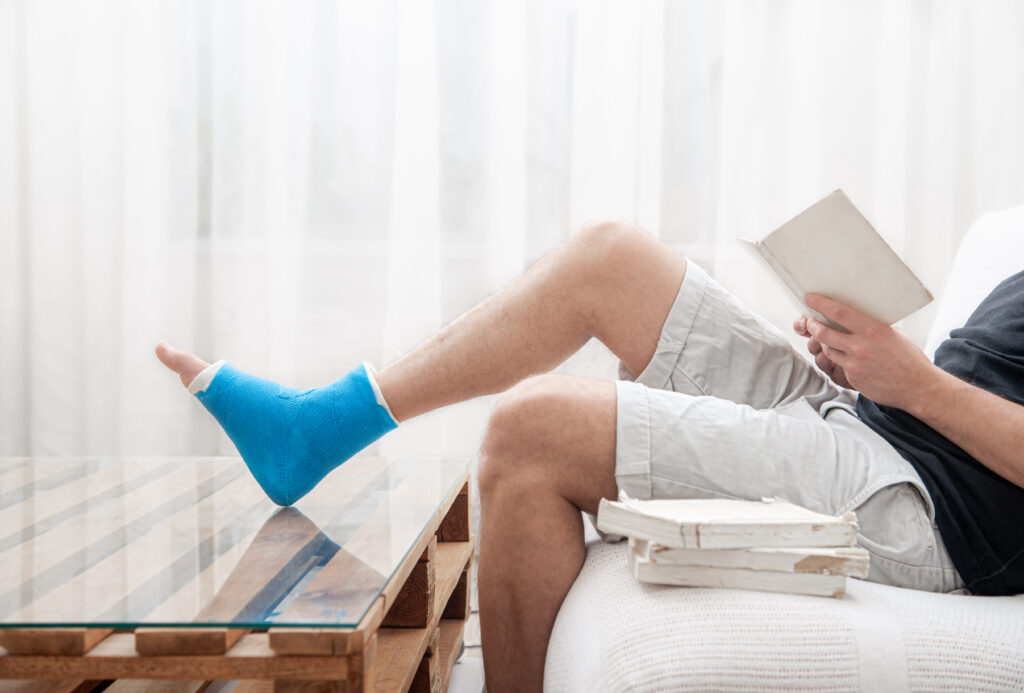 man with broken leg cast reads books against light background interior room.slip and fall accident lawyer