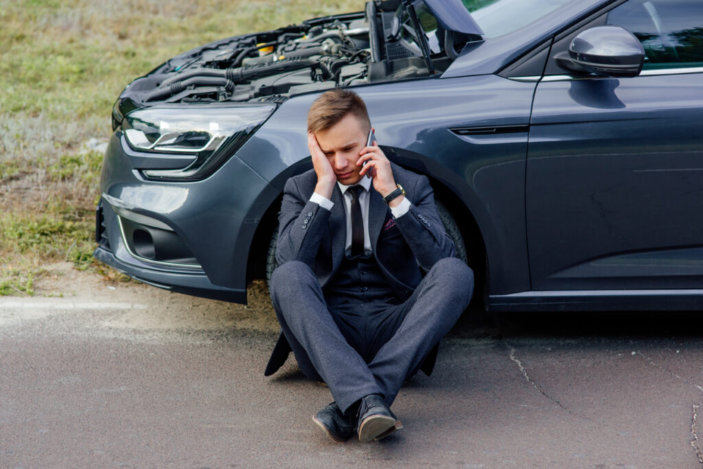 upset businessman use phone sitting road near broken car