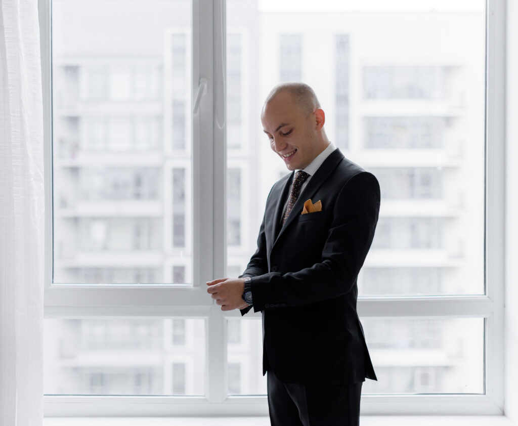 smiled bald man is dressing up near window into stylish suit before important business meeting